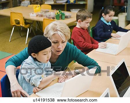 Stock Photo - Teacher and kindergarten student looking at laptop. Fotosearch