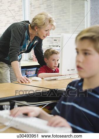 Teacher helping young student in computer lab View Large Photo Image Stock Image - Teacher helping young student in computer lab. Fotosearch