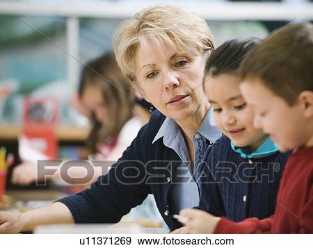 Teacher sitting at table with kindergarten students View Large Photo Image Stock Photo - Teacher sitting at table with kindergarten students. Fotosearch