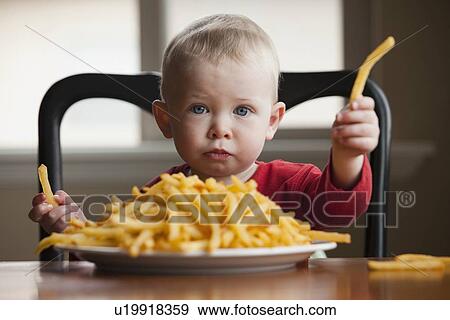 Toddler eating a large plate of French fries View Large Photo Image Stock Photo - Toddler eating a large plate of French fries. Fotosearch