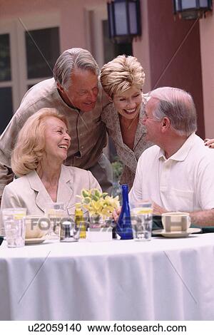 Stock Image - Two senior couples socializing on restaurant patio. Fotosearch