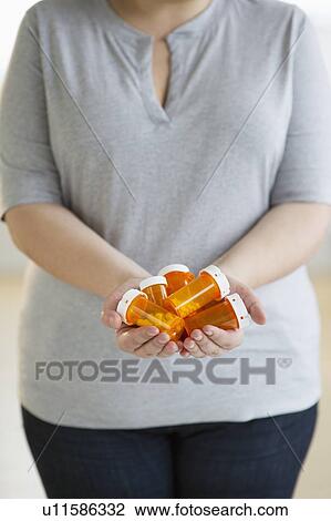 Stock Image - Woman holding several bottles of prescription medication. Fotosearch