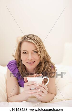 Woman lying down with a cup of coffee View Large Photo Image Stock Photo - Woman lying down with a cup of coffee. Fotosearch