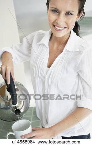 Picture - Woman pouring hot water from kettle. Fotosearch