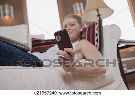 Stock Image - Woman relaxing on sofa while looking at cell phone. Fotosearch