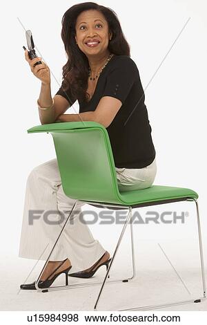 Woman sitting on chair while holding cell phone View Large Photo Image Stock Photo - Woman sitting on chair while holding cell phone. Fotosearch
