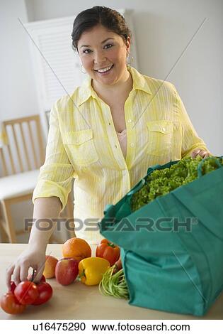 Stock Image - Woman unpacking vegetables from grocery bag. Fotosearch