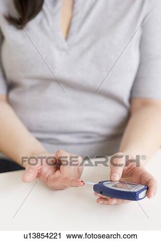 Stock Image - Woman using a blood sugar monitor. Fotosearch