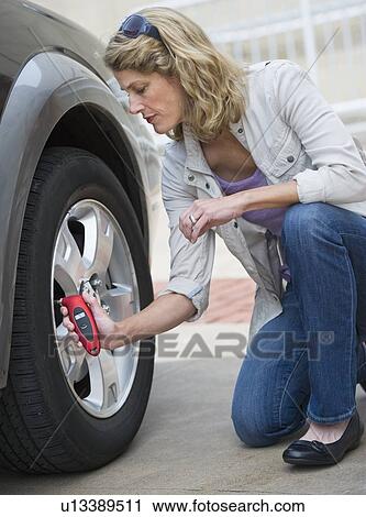 Stock Image - Woman using pressure gauge to check tire pressure. Fotosearch
