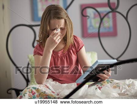 Stock Photo - Young girl crying while looking at photograph. Fotosearch