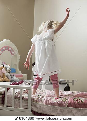 Stock Image - Young girl dancing on her bed. Fotosearch