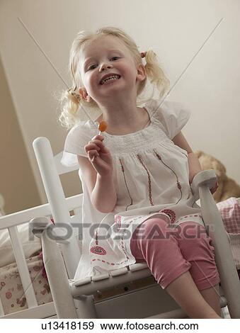 Stock Photo - Young girl in rocking chair eating a sucker. Fotosearch