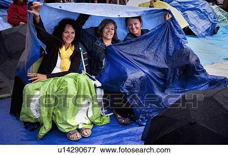 Stock Photo - three ladies at an outdoor music concert (folkfest) protecting themselves under tarps from the rain; edmonton, alberta, canada. Fotosearch