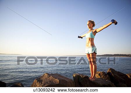 Stock Image - Athletic woman lifting weights outdoors. Fotosearch
