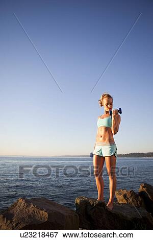 Stock Photo - Athletic woman lifting weights outdoors. Fotosearch