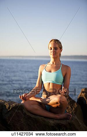 Picture - Athletic woman meditating by the ocean. Fotosearch