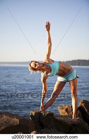 Stock Image - Athletic woman stretching by the ocean. Fotosearch