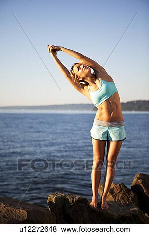 Stock Photo - Athletic woman stretching by the ocean. Fotosearch