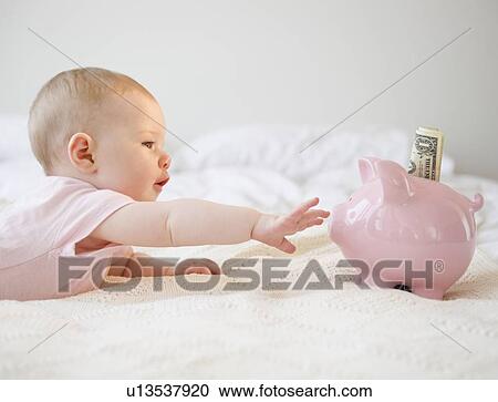 Stock Image - Baby reaching for piggy bank. Fotosearch