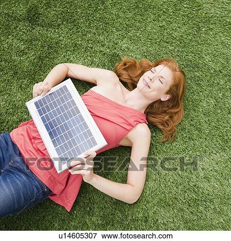 Beautiful woman lying on grass while holding solar panel View Large Photo Image Stock Photo - Beautiful woman lying on grass while holding solar panel. Fotosearch