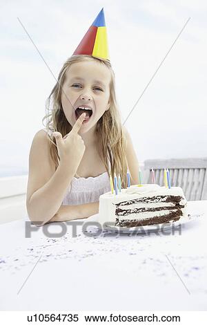 Stock Photography - Birthday girl licking icing off her finger. Fotosearch