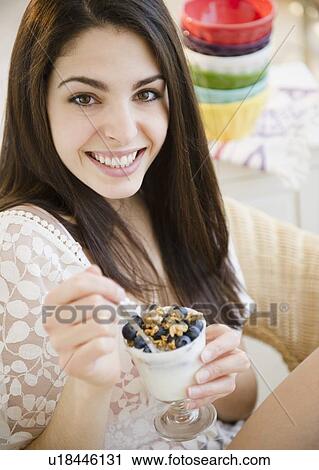 Stock Image - Brunette woman eating granola and yogurt. Fotosearch