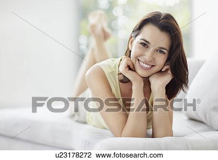 Stock Image - Cheerful brunette woman relaxing on couch. Fotosearch