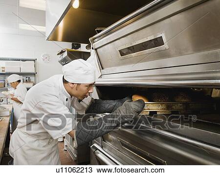 Stock Image - Chef putting bread in oven. Fotosearch