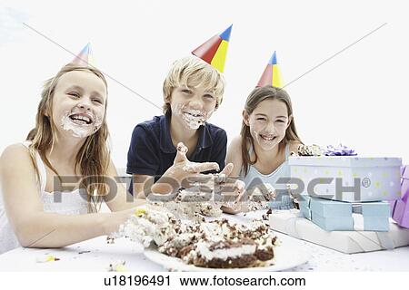 Stock Image - Children eating birthday cake with their hands. Fotosearch
