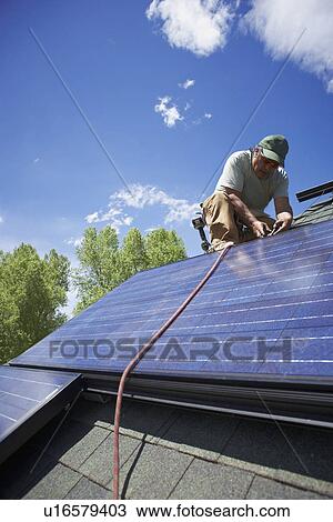 Stock Image - Construction worker installing solar panel on roof. Fotosearch
