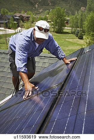 Stock Photo - Construction worker installing solar panel on roof. Fotosearch