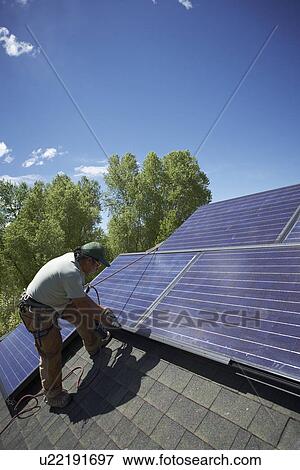 Stock Photo - Construction worker installing solar panel on roof. Fotosearch