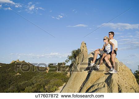 Stock Image - Couple relaxing on peak of rock. Fotosearch