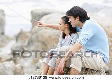 Couple sitting on rock by the sea View Large Photo Image Stock Photography - Couple sitting on rock by the sea. Fotosearch