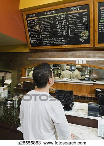 Stock Image - Customer reading chalkboard menu. Fotosearch