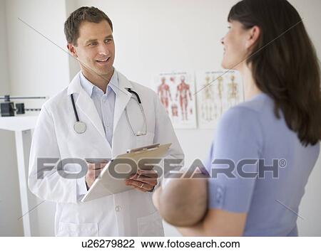 Stock Image - Doctor talking to woman in examination room. Fotosearch