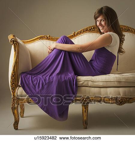 Stock Image - Elegant woman sitting on antique sofa. Fotosearch