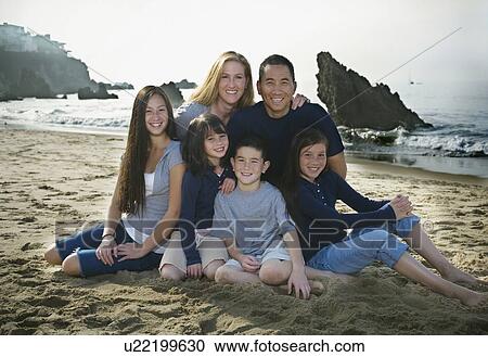 Stock Image - Family sitting together at the beach. Fotosearch