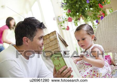 Stock Image - Father helping his daughter paint a birdhouse. Fotosearch
