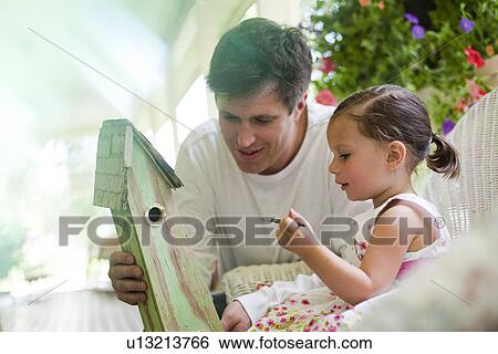 Stock Photograph - Father helping his daughter paint a birdhouse. Fotosearch