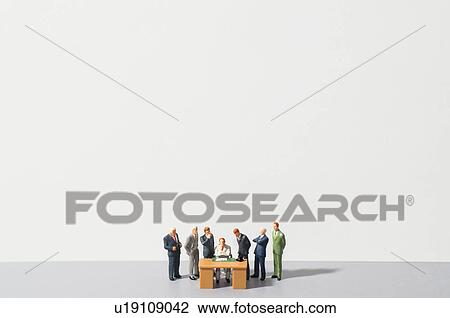 Stock Image - Figurines of people standing around desk. Fotosearch