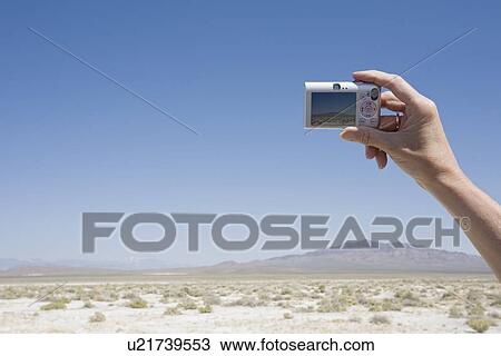 Stock Image - Hand holding a camera in the desert. Fotosearch
