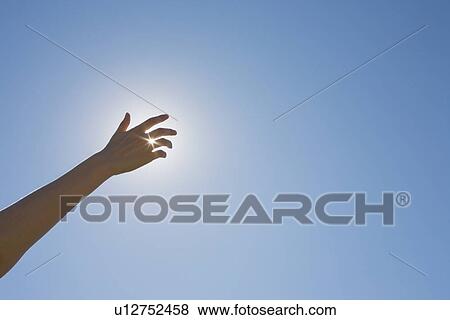 Stock Photo - Hand in front of a sun flare in the sky. Fotosearch