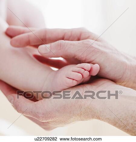 Stock Image - Hands cradling baby's foot. Fotosearch