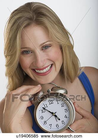 Stock Photography - Happy blond woman holding an alarm clock. Fotosearch