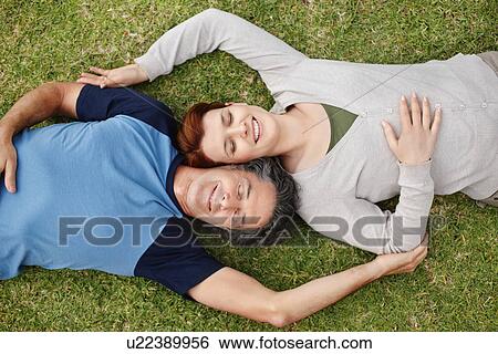 Happy couple relaxing on the grass together View Large Photo Image Stock Photograph - Happy couple relaxing on the grass together. Fotosearch