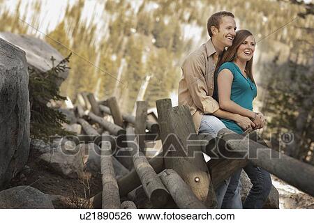 Happy couple sitting on log fence View Large Photo Image Stock Photograph - Happy couple sitting on log fence. Fotosearch