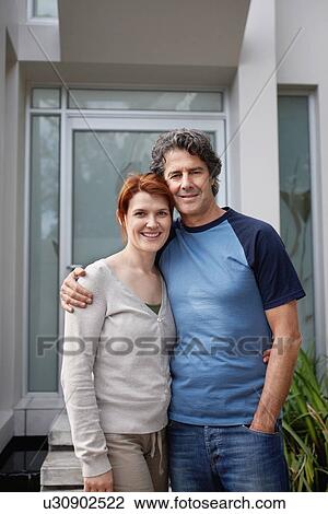 Stock Image - Happy couple standing with their arms around one another. Fotosearch