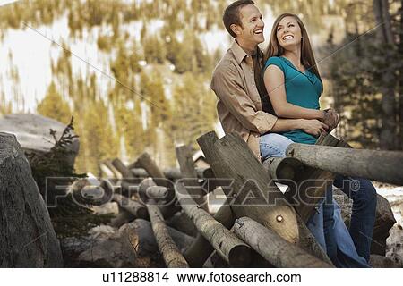 Picture - Laughing couple sitting on log fence. Fotosearch