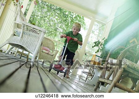Stock Photo - Little boy riding scooter on porch. Fotosearch